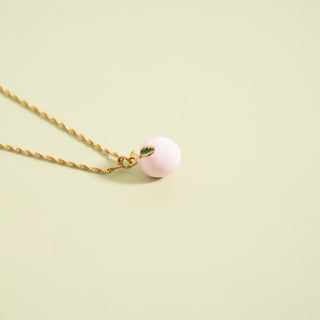 Necklace with a pink peach pendant on a light green background