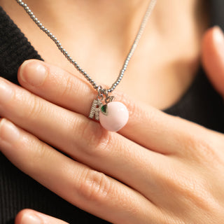 Necklace with a pink peach pendant and small charms held by a hand