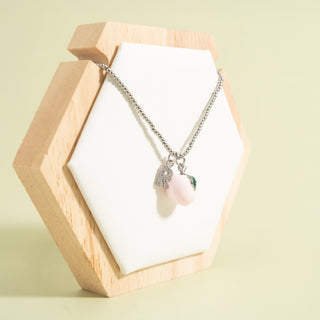 Necklace with a pink peach pendant on a wooden stand against a light green background