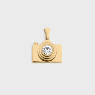 Gold camera-shaped pendant with a central gemstone on a light gray background