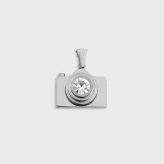 Silver camera-shaped pendant with a central gemstone on a light gray background