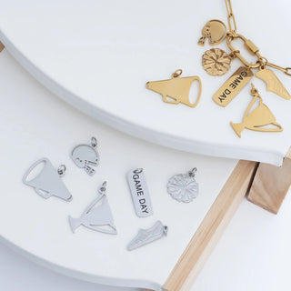 Gold and silver charms on a white surface with a wooden stick.