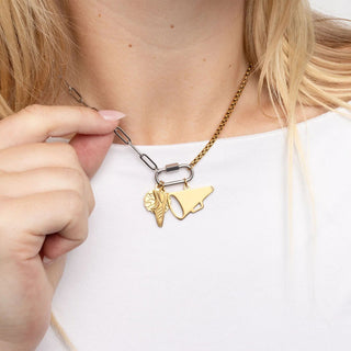 Gold necklace with two charms being adjusted by a hand on a white background