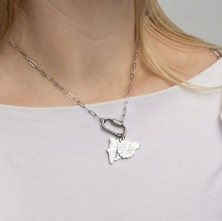 Silver necklace with a leaf pendant worn by a person on a plain background