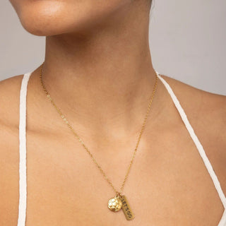 Gold necklace with a pendant on a person wearing a white top against a neutral background
