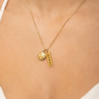 Gold necklace with a 'LET'S GO' tag and round pendant on a person's neck.