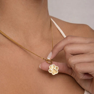 Gold necklace with a paw-shaped pendant being adjusted on a person's neck.