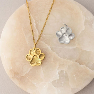 Gold and silver paw print pendants on a marble surface
