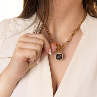 Gold necklace with a pendant worn by a person against a neutral background
