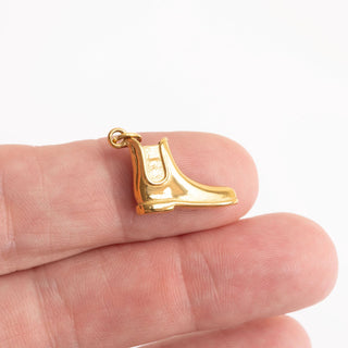 Gold equestrian boot pendant held between fingers on a white background