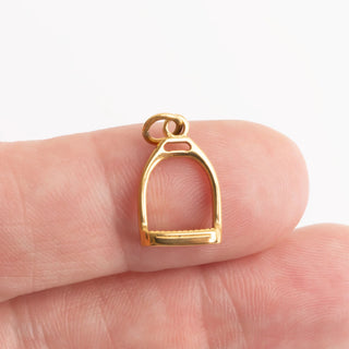Gold stirrup charm held between fingers on a white background