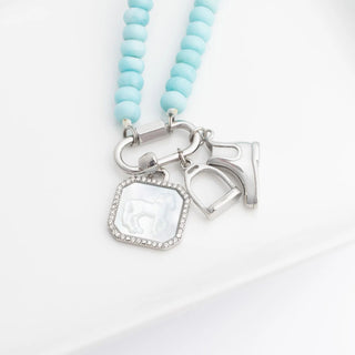 Necklace with light blue beads and silver equestrian charms on a white background