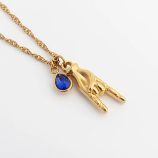 Gold necklace with a blue gemstone and hand-shaped pendant on a white background