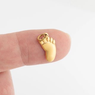 Gold foot-shaped charm on a finger against a white background