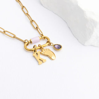 Gold necklace with a baby foot, birthstone, and initial charms on a white background