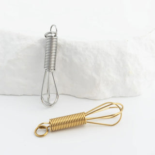 Two whisks, one silver and one gold, on a white background.