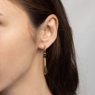 Gold whisk-shaped earring worn by a person with a neutral background