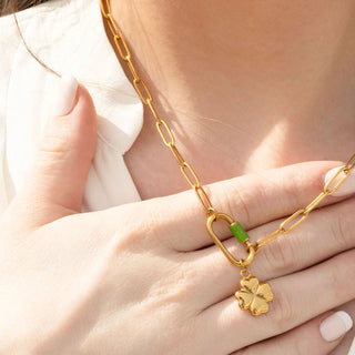 Gold chain necklace with a clover pendant held by a hand