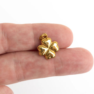Gold four-leaf clover pendant held between fingers on a white background