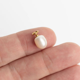 Pearl pendant on a gold chain held by fingers against a white background