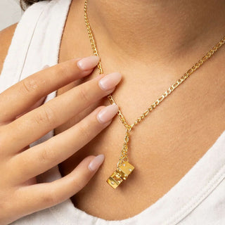Gold necklace with a dice pendant worn by a person, with a hand touching the necklace.