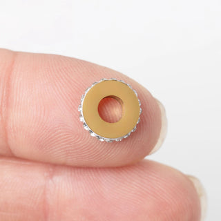 Gold stone spacer bead held between fingers against a white background