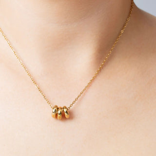 Gold necklace with three spacer beads on a person's neck against a neutral background