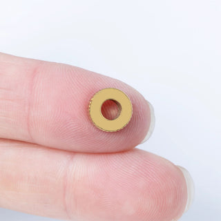 Gold fluted spacer beads held between fingers against a white background