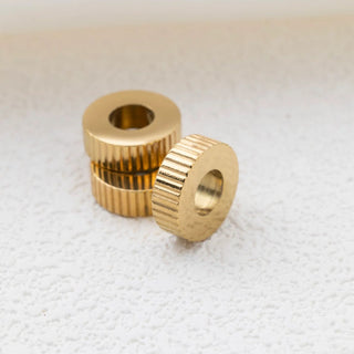 Two gold fluted spacer beads on a textured white surface