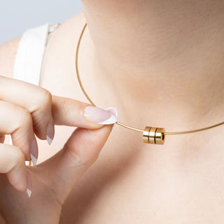 Gold necklace with spacer beads being adjusted on a person's neck with a neutral background