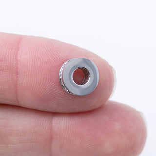 Silver spacer bead on a finger against a white background