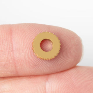 Gold textured spacer bead on a finger against a white background