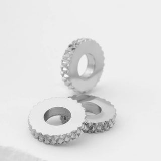 Two silver textured spacer beads on a light gray background