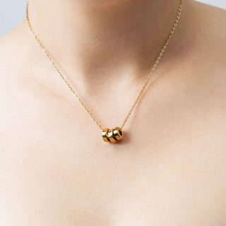 Gold necklace with spacer bead on a person's neck against a neutral background