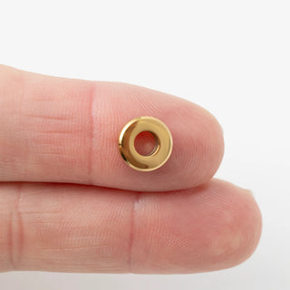 Gold spacer bead held between fingers on a white background