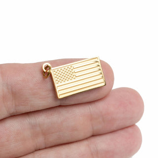 Gold American flag pendant held between fingers on a white background