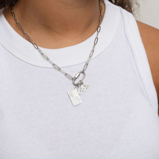 Silver chain necklace with charms worn by a person in a white tank top.