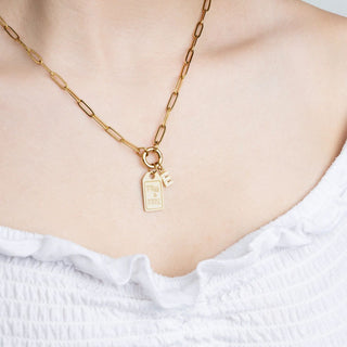 Gold necklace with a tag pendant on a person wearing a white top