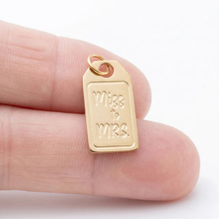 Gold 'Miss to Mrs.' pendant held between fingers on a white background