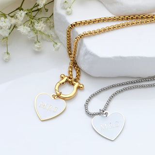 Two necklaces with heart-shaped 'MRS' charms on a white surface with flowers.