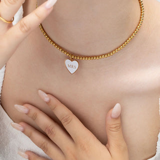 Gold necklace with a heart-shaped 'MRS' pendant on a person's chest.
