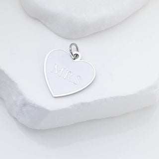 Silver heart-shaped pendant with 'MRS' engraving on a marble surface