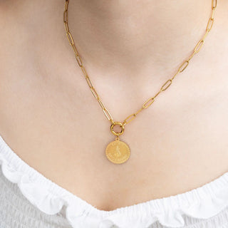 Gold chain necklace with a round pendant on a person wearing a white top.