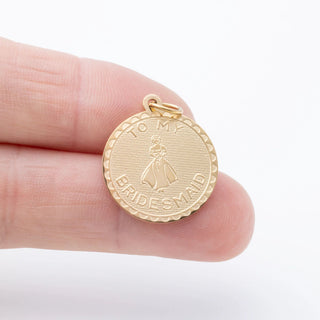 Gold 'to My Bridesmaid' pendant held between fingers on a white background