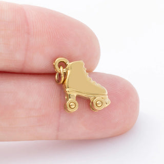 Gold roller skate charm held between fingers on a white background