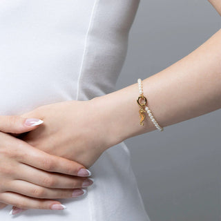 Pearl bracelet with a gold charm on a wrist against a neutral background