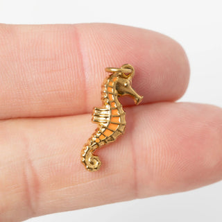 Gold seahorse pendant held between two fingers on a white background