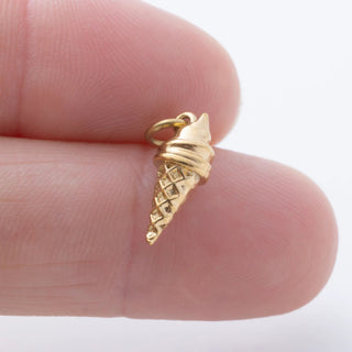 Gold ice cream cone pendant held between fingers on a white background