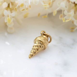 Gold ice cream cone-shaped pendant on a marble surface with flowers in the background