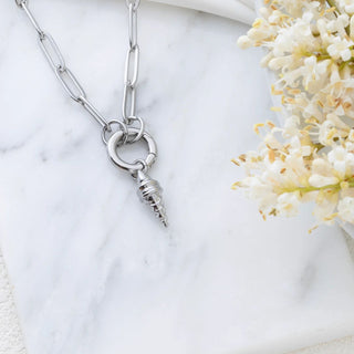 Silver necklace with a unique pendant on a marble surface with flowers
